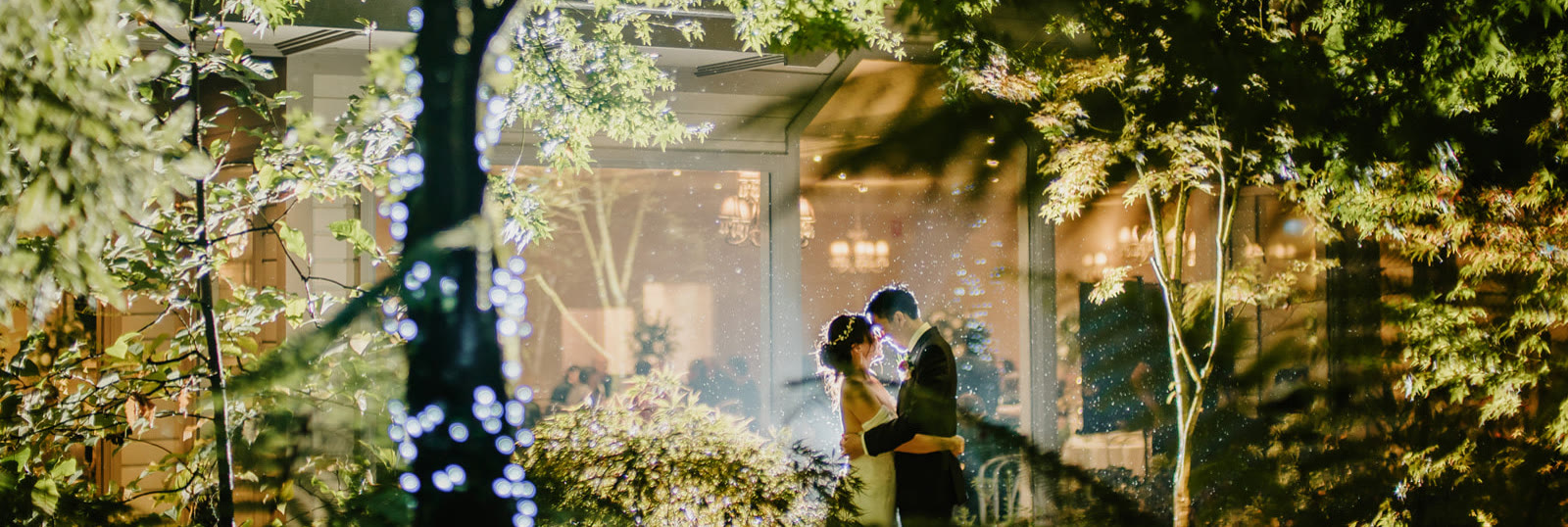 A couple outside the lit dining room at night.