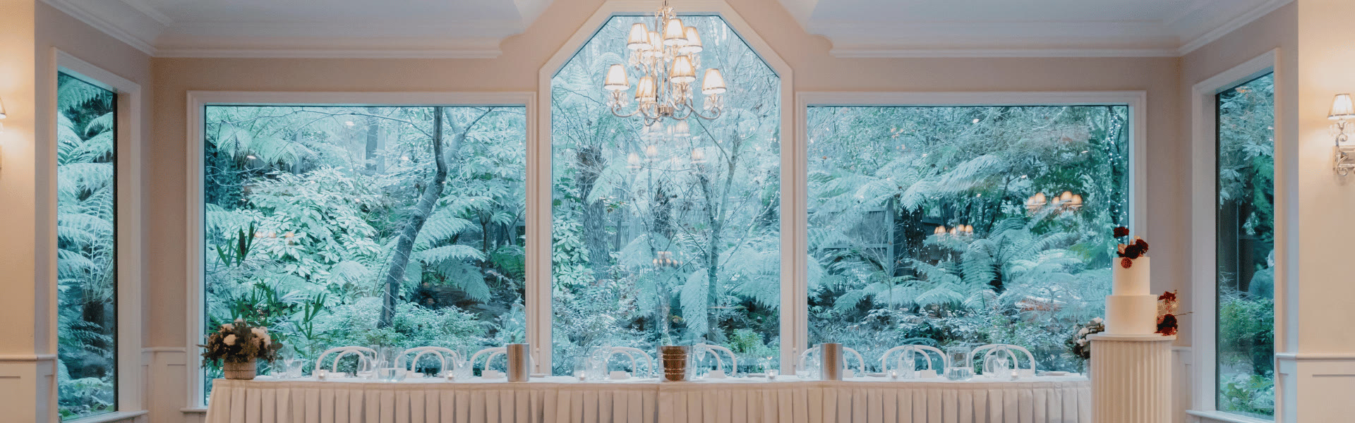 A long bridal table beneath windows opening onto the fernery.